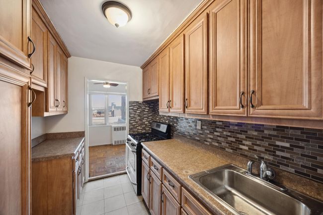 Kitchen featuring brown cabinets, tasteful backsplash, a ceiling fan, a sink, and gas range | Image 4