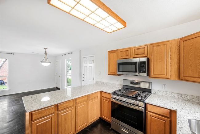 Kitchen featuring appliances with stainless steel finishes, a peninsula, light stone countertops, dark wood-style flooring, and brown cabinetry | Image 12