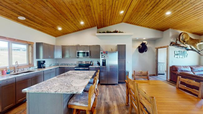 Kitchen with light stone counters, wood ceiling, stainless steel appliances, a sink, and a center island | Image 5