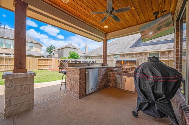 Step outside to a beautifully crafted outdoor patio complete with a gas fire pit, kitchen/bar setup, built-in gas grill, and refrigerator—perfect for entertaining or relaxing. | Image 37