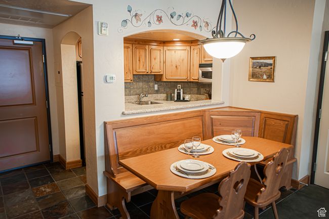 Kitchen featuring arched walkways, light countertops, tasteful backsplash, stainless steel microwave, and decorative light fixtures | Image 6