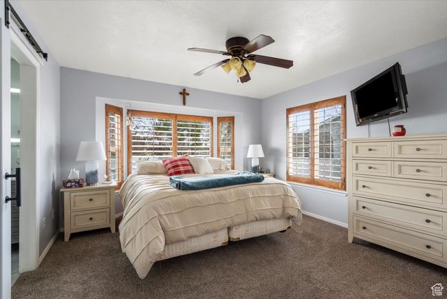 Bedroom with dark colored carpet, baseboards, a barn door, and ceiling fan | Image 16