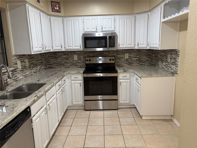 Kitchen with stainless steel appliances, decorative backsplash, a sink, light tile patterned flooring, and light stone countertops | Image 7