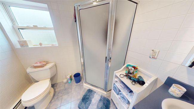 Full bathroom featuring tile walls, a shower stall, healthy amount of natural light, tile patterned floors, and baseboard heating | Image 18