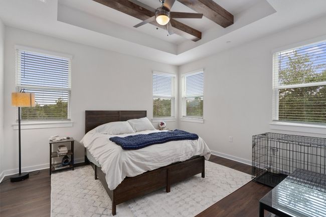 Bedroom with a raised ceiling, dark wood-style floors, multiple windows, beam ceiling, and ceiling fan | Image 27