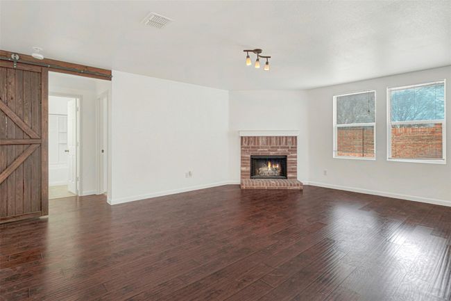 Unfurnished living room featuring a barn door, dark wood-type flooring, baseboards, and a fireplace | Image 7