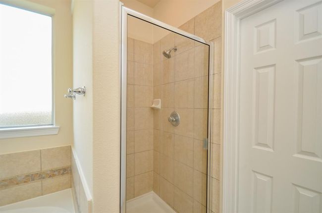 This photo shows a clean, modern bathroom with a tiled walk-in shower featuring a glass door. There's a frosted window for natural light and privacy, and a bathtub with decorative tile accents. | Image 21