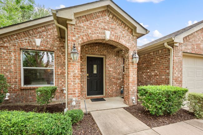 Covered front porch with brick archway and decorative sconces, leading to a classic black front door – perfect for a warm welcome. | Image 5