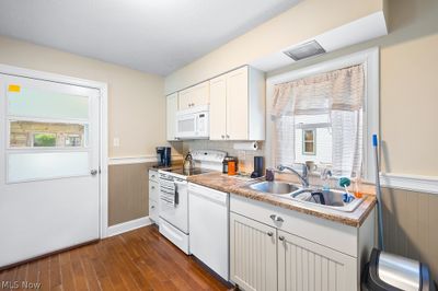 Kitchen featuring decorative backsplash, white cabinets, white appliances, sink, and dark wood-type flooring | Image 3