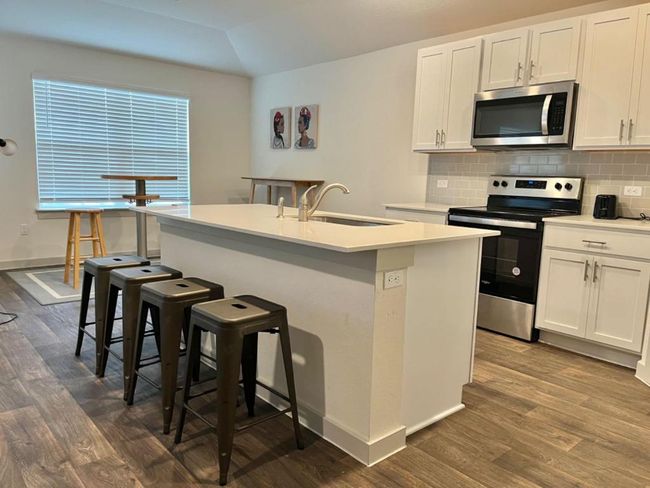 Kitchen with appliances with stainless steel finishes, dark wood finished floors, a sink, a kitchen island with sink, and a breakfast bar | Image 9