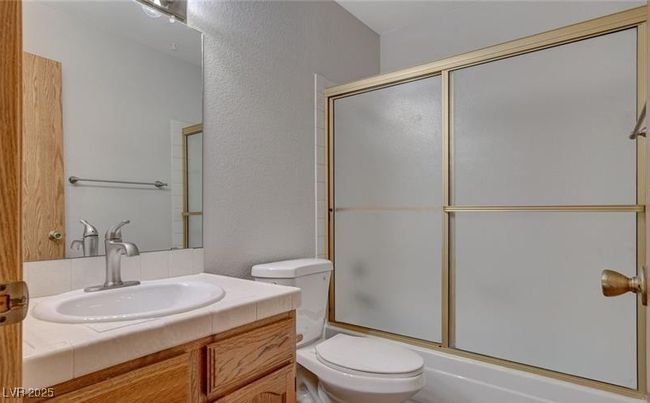Full bath with toilet, vanity, enclosed tub / shower combo, and a textured wall | Image 11