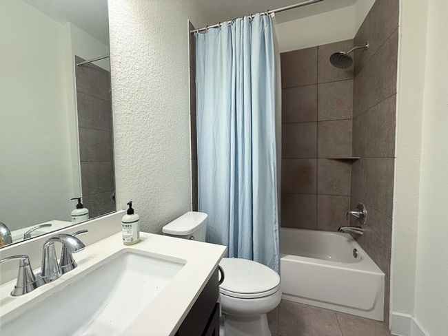 Bathroom featuring a textured wall, toilet, shower / bath combo with shower curtain, vanity, and tile patterned flooring | Image 12