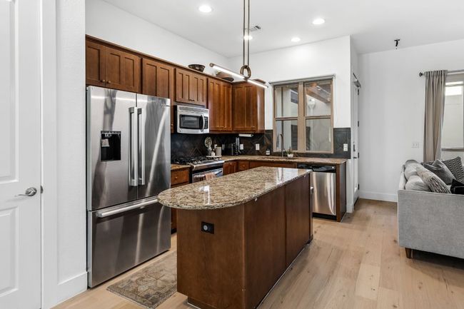 Kitchen with a center island, light wood-type flooring, decorative backsplash, light stone counters, and appliances with stainless steel finishes | Image 10