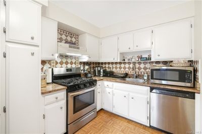 Kitchen featuring light parquet flooring, white cabinetry, sink, decorative backsplash, and appliances with stainless steel finishes | Image 2