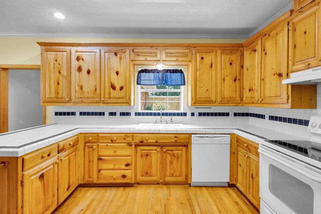 Kitchen with white appliances, under cabinet range hood, decorative backsplash, crown molding, and light wood-style floors | Image 8