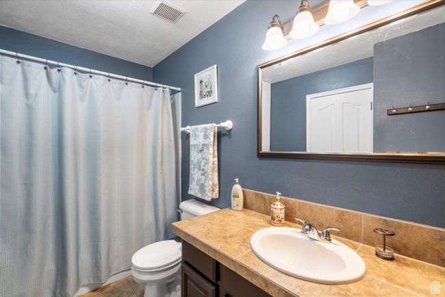 Full bath with a textured ceiling, visible vents, a shower with shower curtain, toilet, and vanity | Image 15