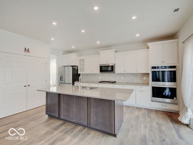 Kitchen featuring recess can lighting, island w/ sink, laminate flooring, stainless steel appliances including double oven, gas cooktop, microwave w/ hood vented to outside, dishwasher, refrigerator, & pantry | Image 18