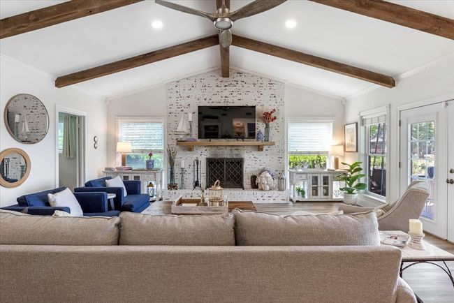 Living area featuring a fireplace, lofted ceiling with beams, ceiling fan, a healthy amount of sunlight, and wood finished floors | Image 7