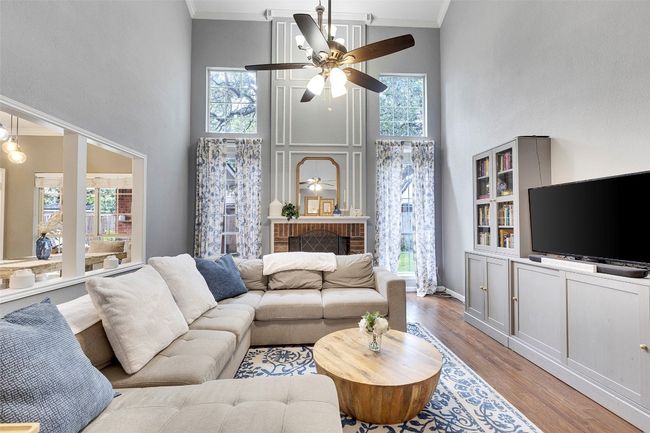 Living area with ceiling fan, a towering ceiling, crown molding, wood finished floors, and baseboards | Image 4