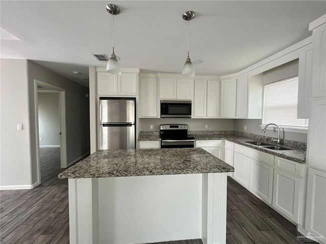 Kitchen featuring stainless steel appliances, dark wood finished floors, a kitchen island, and dark stone counters | Image 4