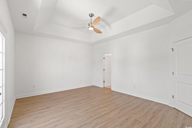 Empty room with a raised ceiling, ceiling fan, and light wood-style flooring | Image 13