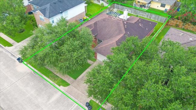 This aerial photo shows a spacious single-story home surrounded by mature trees. The property is outlined in green, indicating its generous lot size. It features a fenced backyard and is situated in a neighborhood with nearby homes. | Image 32