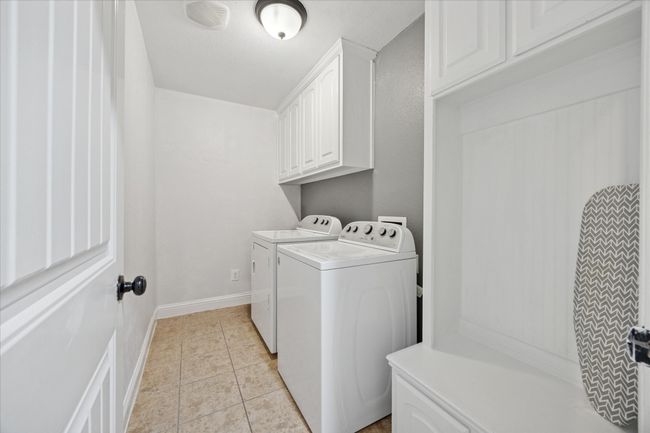 Laundry room featuring washer and dryer, light tile patterned floors, cabinet space, and baseboards | Image 23