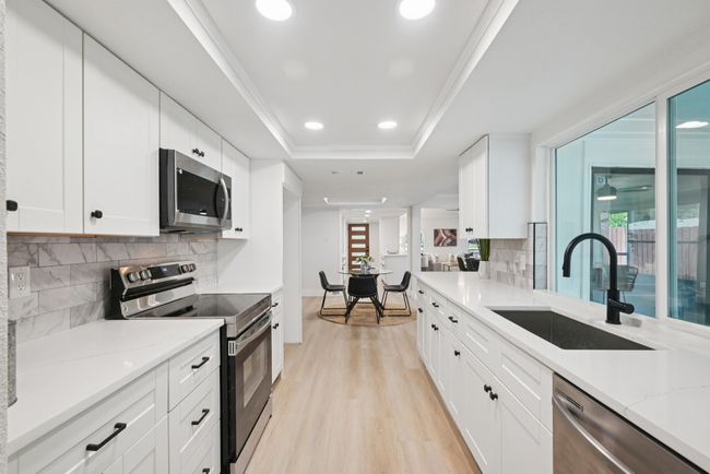 Kitchen featuring stainless steel appliances, a tray ceiling, light wood-style flooring, tasteful backsplash, and light stone counters | Image 24