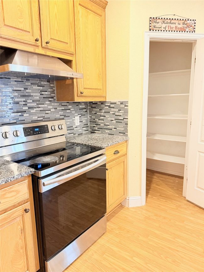 Kitchen with stainless steel range with electric cooktop, ventilation hood, light wood-type flooring, and light brown cabinetry | Image 13