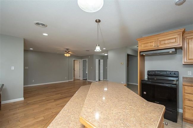 Kitchen with black range with electric stovetop, light wood-style flooring, a ceiling fan, under cabinet range hood, and a kitchen island | Image 14