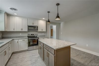 Kitchen featuring light hardwood / wood-style floors, stainless steel appliances, light stone counters, a kitchen island, and hanging light fixtures | Image 3