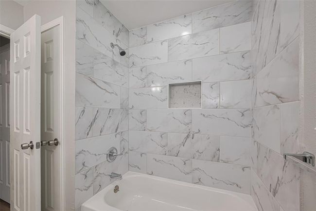 This full bathroom includes a tub-shower combo surrounded by the same tasteful gray-and-white tilework seen throughout. | Image 24