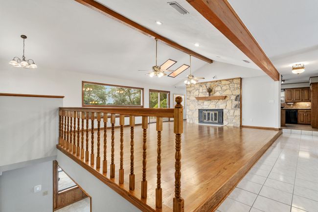 Stairs featuring visible vents, lofted ceiling with beams, a ceiling fan, tile patterned flooring, and a stone fireplace | Image 25