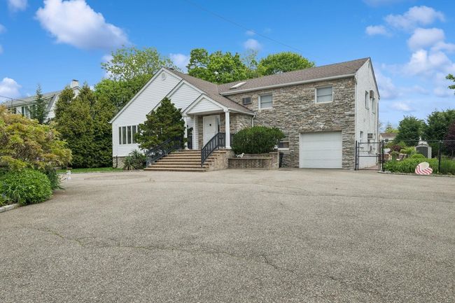 View of front facade with stone siding, a gate, driveway, a garage, and fence | Image 39