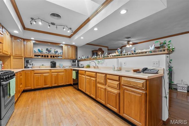 Kitchen featuring crown molding, open shelves, gas stove, light wood-type flooring, and a raised ceiling | Image 65