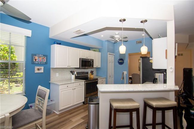 Kitchen features white cabinetry, light colored stone counters, pendant and recessed lighting and stainless steel appliances. | Image 12