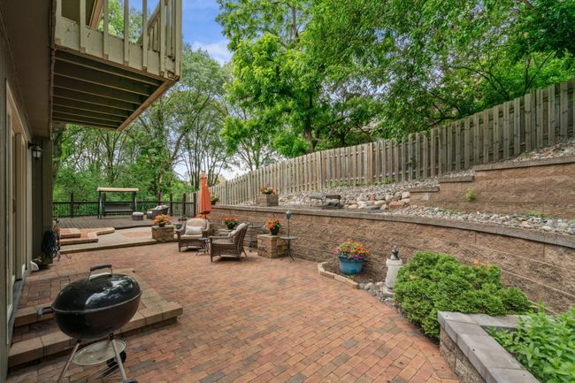 Expansive brick patio surrounded by tiered retaining walls, lush landscaping, and mature trees—perfect for relaxing or entertaining outdoors. | Image 19