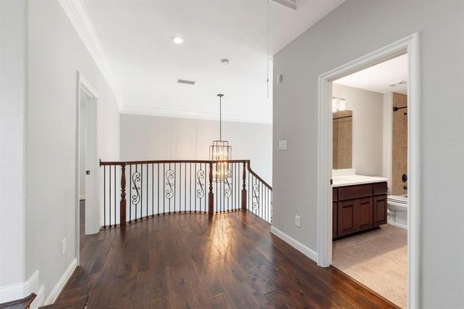 Warm hardwood floors and wrought iron detailing elevate this upstairs landing, where natural light pours in from below and a full bath adds convenience for the adjacent bedrooms. | Image 28