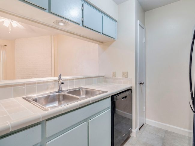 Kitchen featuring tile countertops, dishwashing machine, a sink, baseboards, and light tile patterned flooring | Image 6