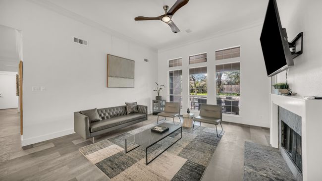 Living area featuring crown molding, ceiling fan, a fireplace with flush hearth, a high ceiling, and wood finished floors | Image 5