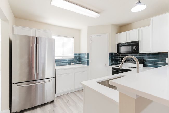 Kitchen with black microwave, freestanding refrigerator, light countertops, white cabinetry, and backsplash | Image 7