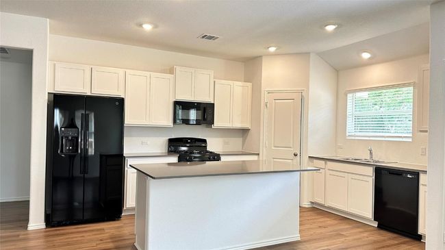 Kitchen with visible vents, a sink, white cabinets, black appliances, and light wood finished floors | Image 14