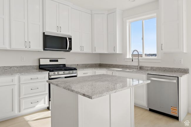 Kitchen with appliances with stainless steel finishes, light stone countertops, white cabinetry, a kitchen island, and light wood finished floors | Image 8