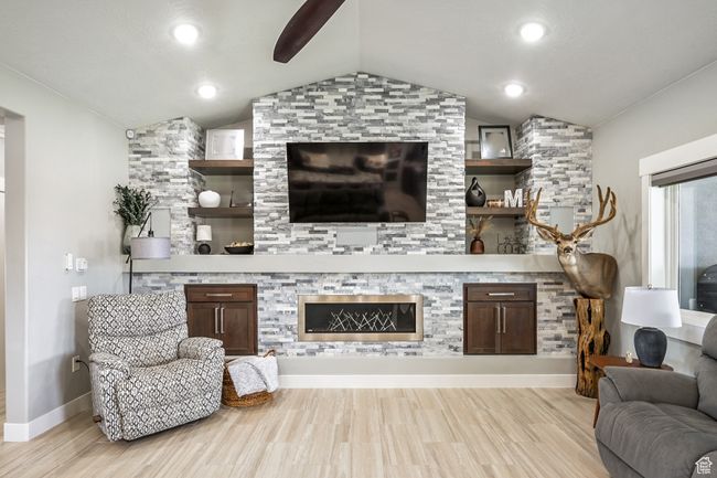 Living room with vaulted ceiling, light wood finished floors, a ceiling fan, and a glass covered fireplace | Image 13