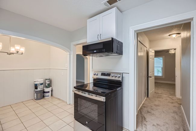 Kitchen featuring visible vents, stainless steel electric range oven, ceiling fan, and white cabinets | Image 14