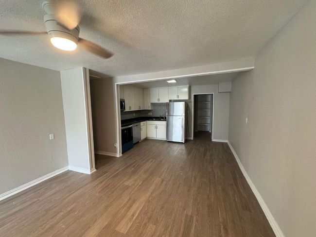 Unfurnished living room with a sink, dark wood-type flooring, baseboards, a textured ceiling, and ceiling fan | Image 5