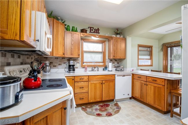 Kitchen with a peninsula, light countertops, tasteful backsplash, and white appliances | Image 15
