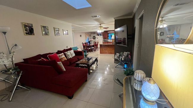 Living room with ceiling fan, ornamental molding, a skylight, and light tile patterned floors | Image 6