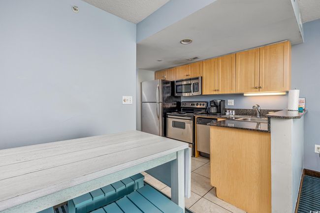 Kitchen featuring dark stone countertops, light tile patterned floors, stainless steel appliances, and a sink | Image 10