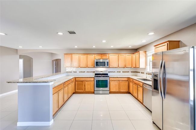 Kitchen featuring stainless steel appliances, light brown cabinets, a peninsula, light stone countertops, and arched walkways | Image 11
